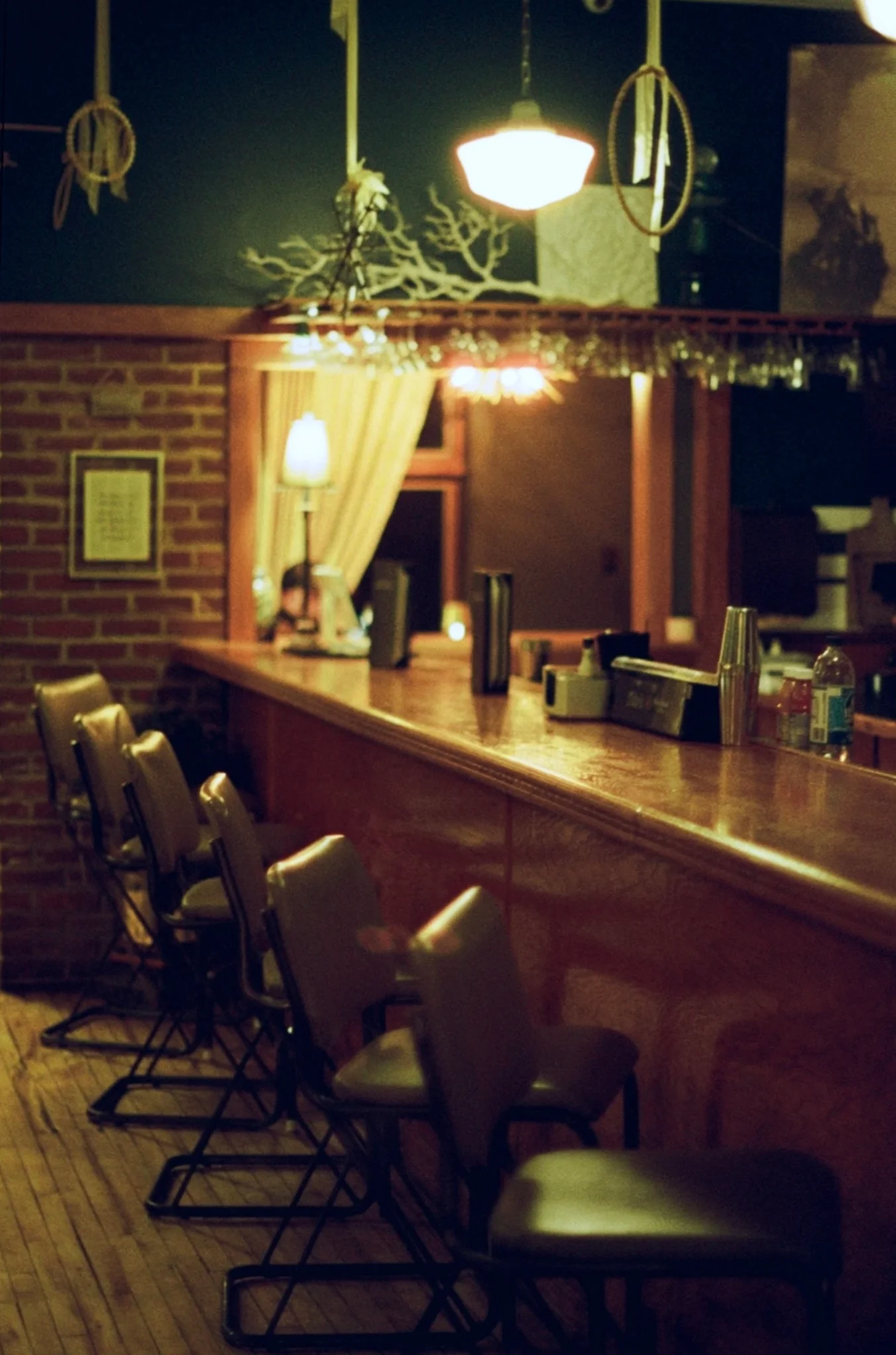 A cozy dining area with several wooden tables and chairs, featuring large windows and a decorative tree. The walls are a deep green, and artwork is displayed.
