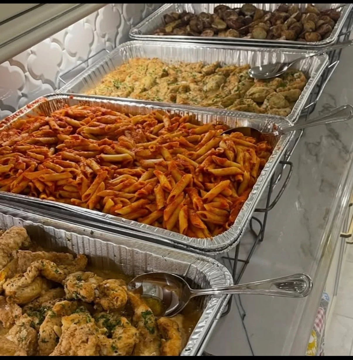 Buffet trays with pasta, chicken, and meatballs in a restaurant setting.