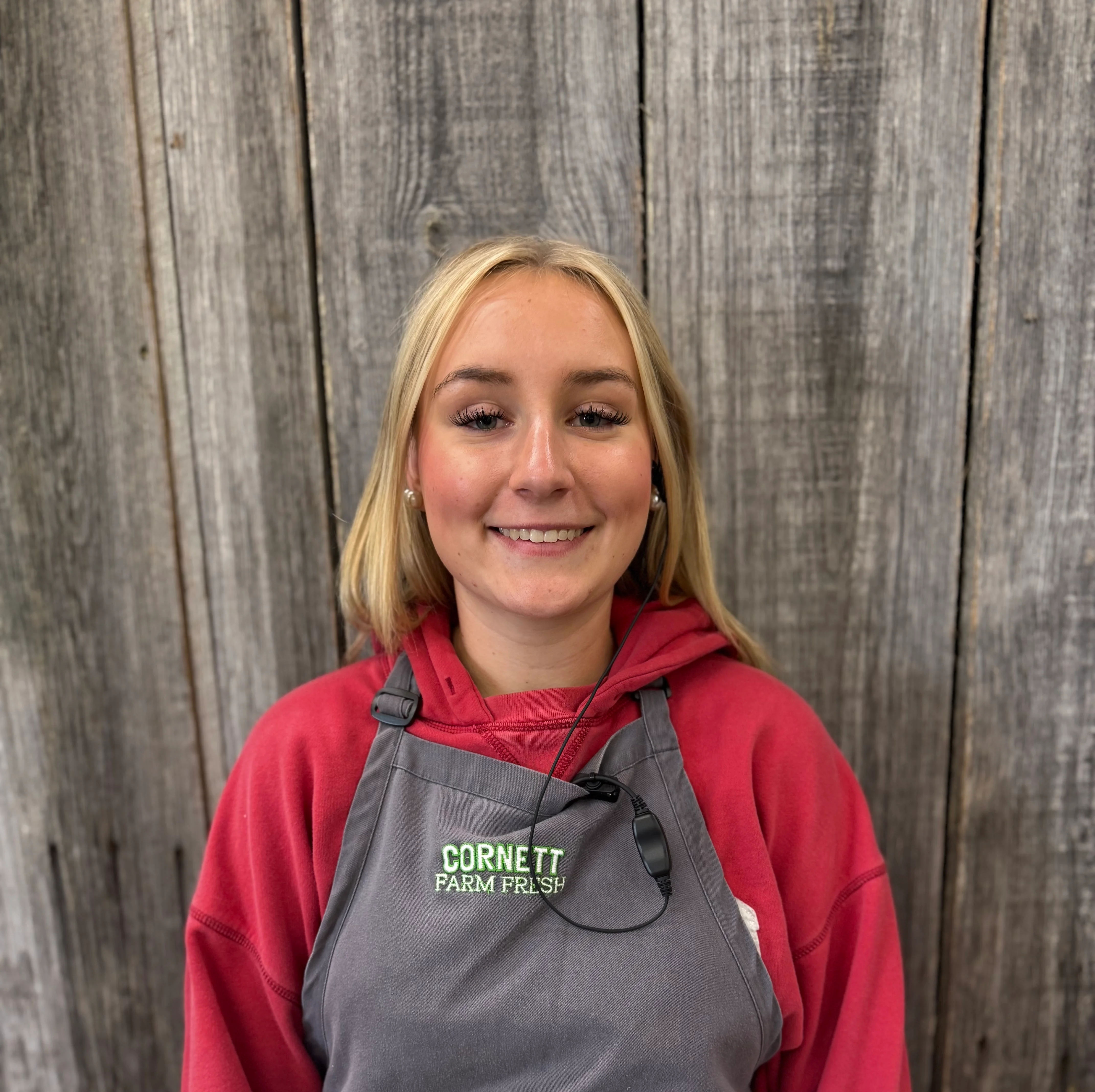 Smiling restaurant worker wearing a gray apron against a rustic wood backdrop