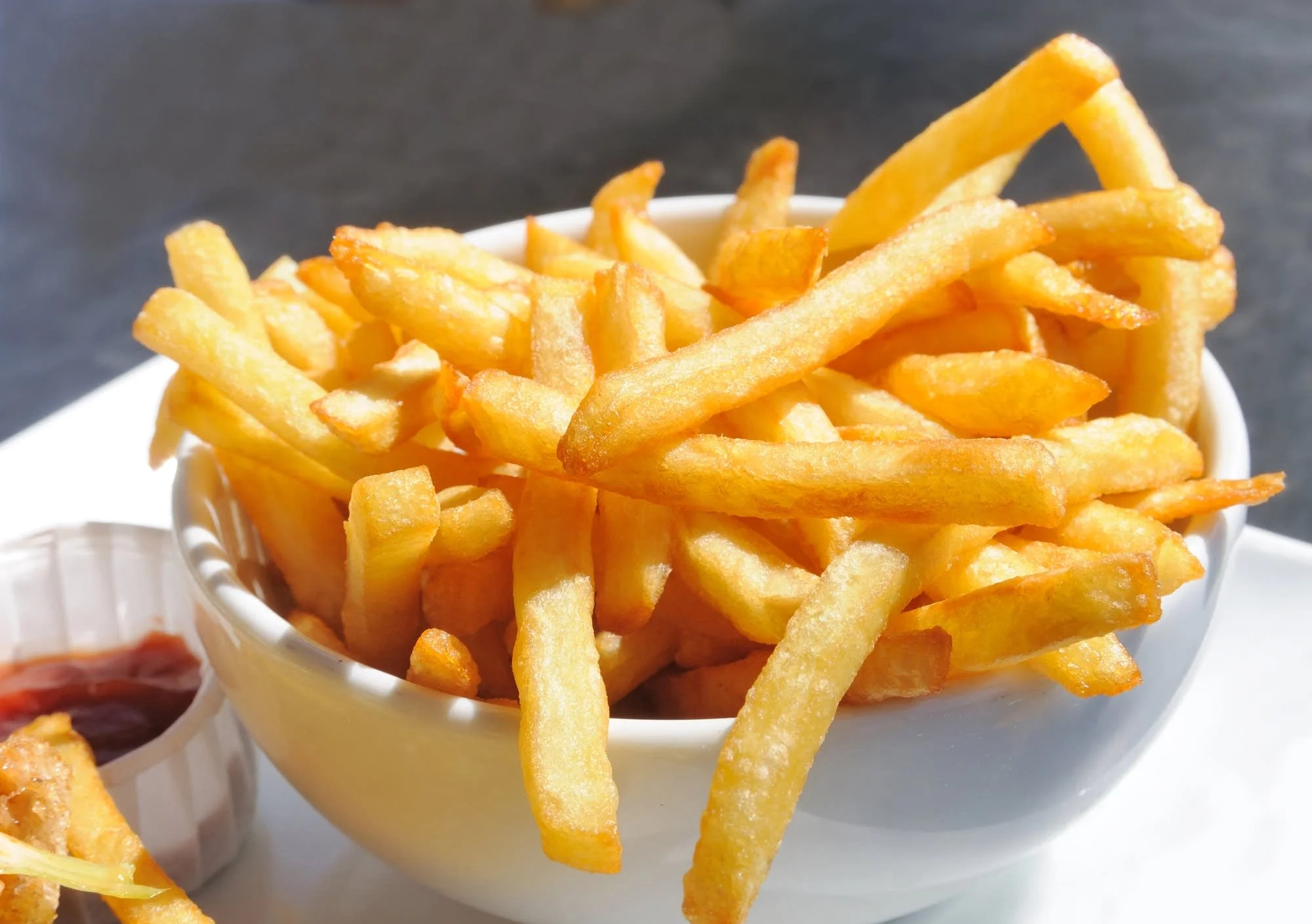 A bowl overflowing with golden, crispy French fries, served with a side of ketchup.