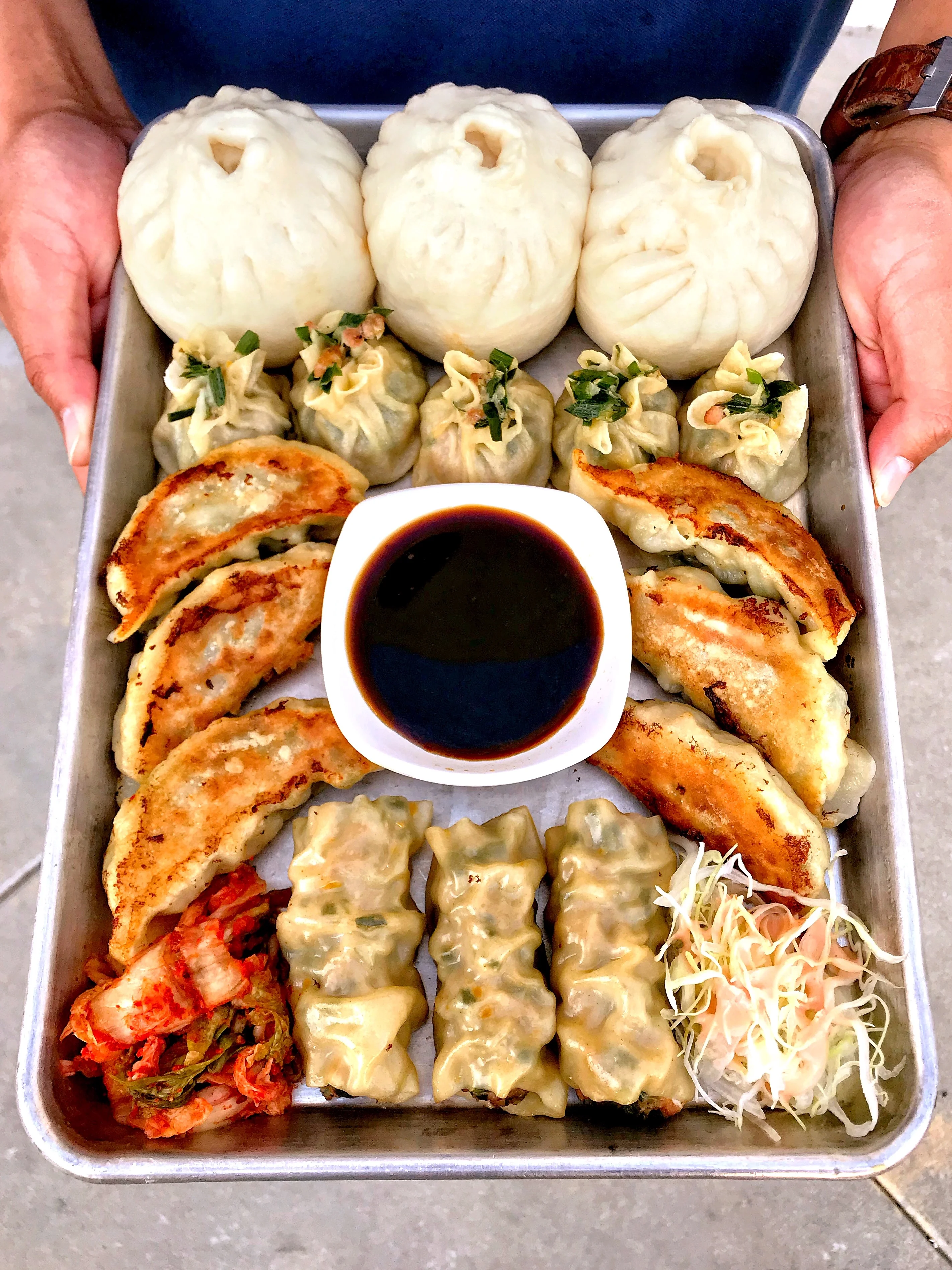 A tray of assorted dumplings, bao buns, and dipping sauce.