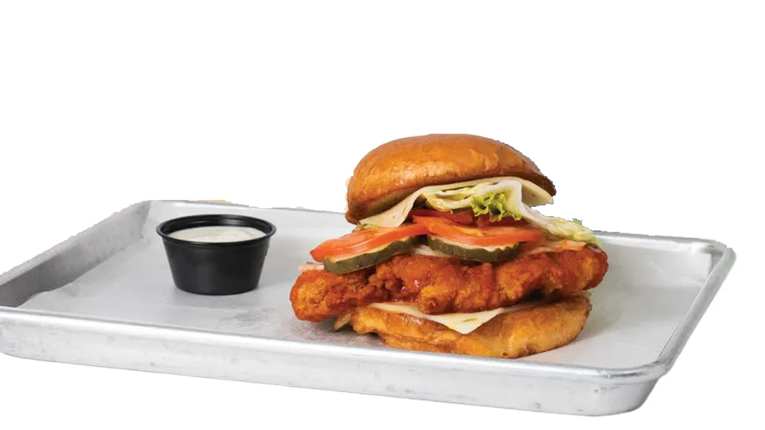 Crispy chicken sandwich with lettuce, tomato, and pickles on a tray.
