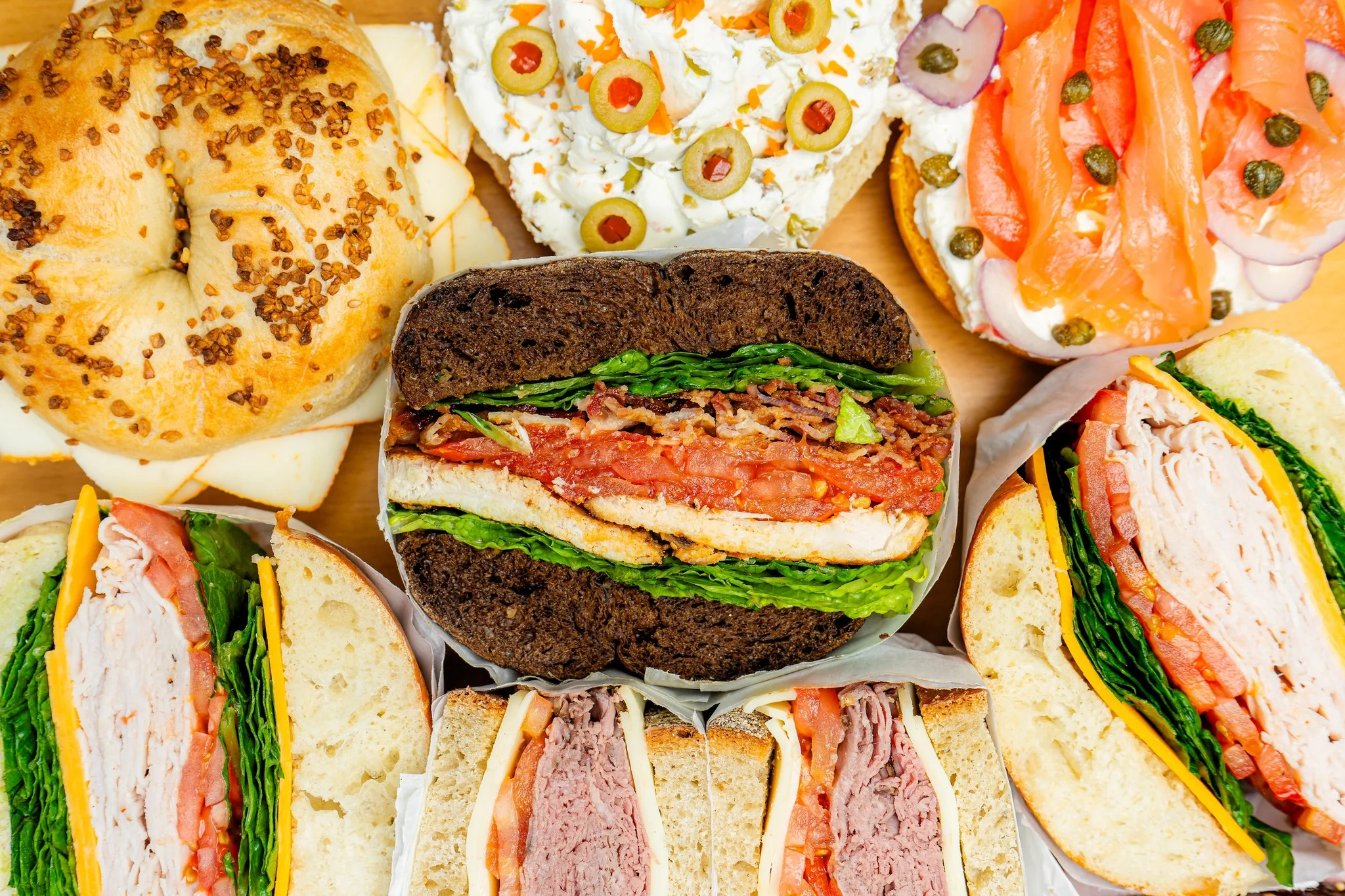 Assorted deli sandwiches and bagels on a wooden platter