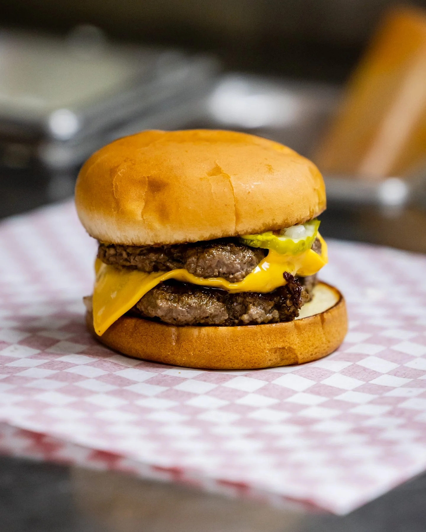 A delicious cheeseburger featuring two beef patties, melted cheese, and a soft bun, presented on a checkered paper.