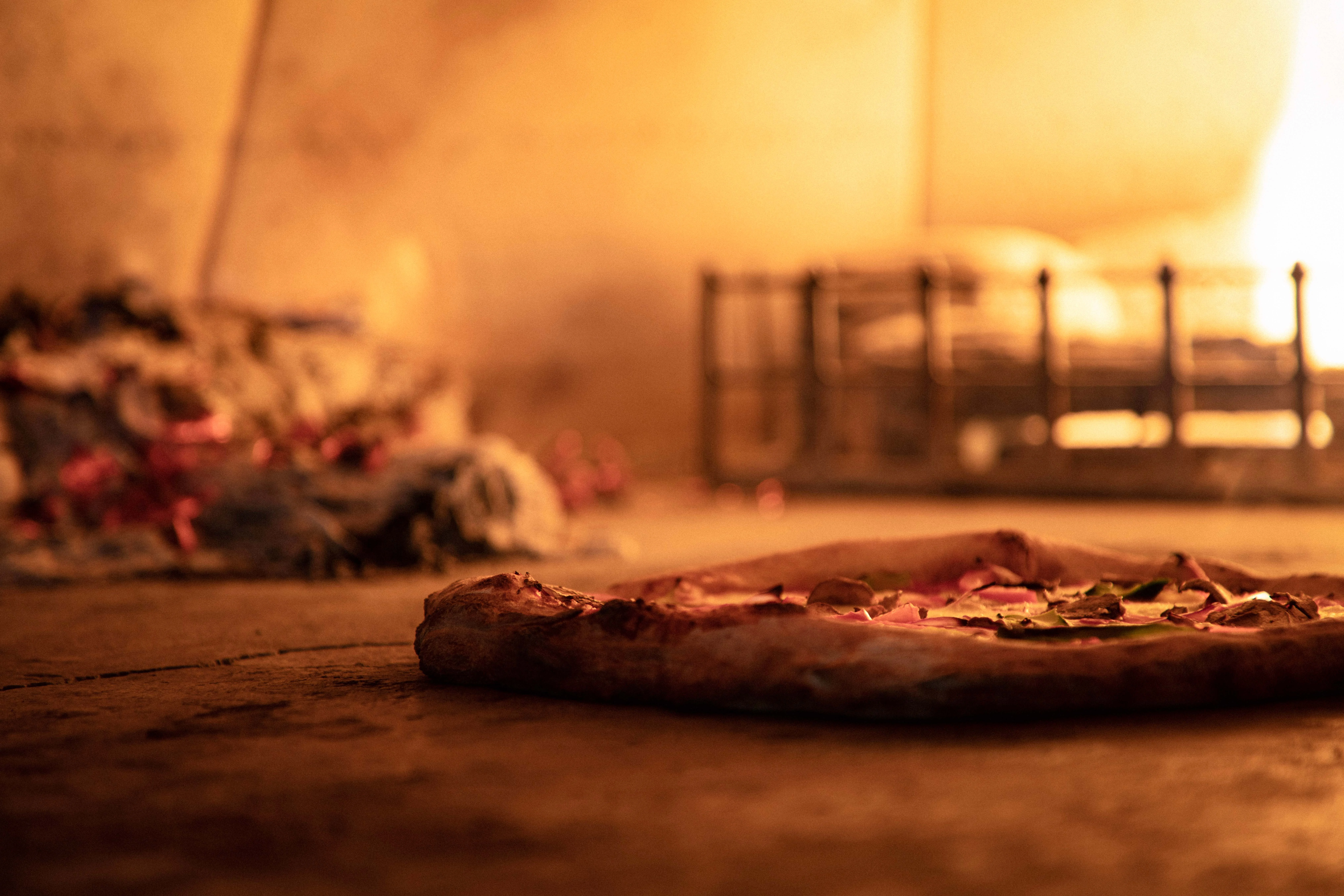 Pizza in wood burning oven with fire in background