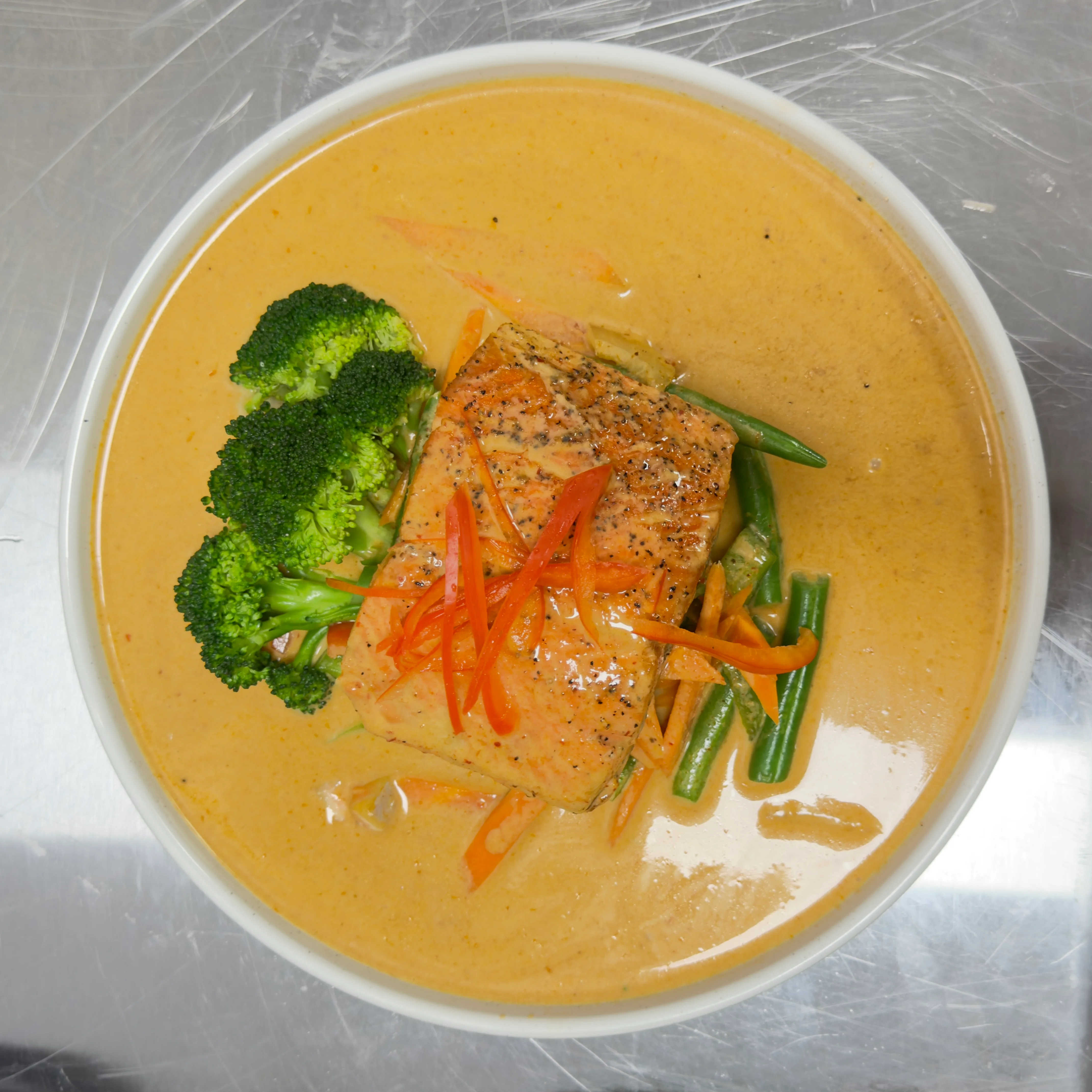 A bowl of salmon served in a creamy coconut sauce with broccoli, green beans, and garnished with thin strips of carrot.