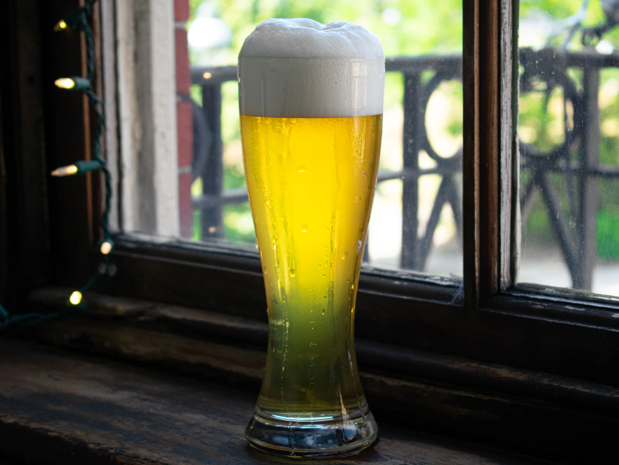Chilled glass of golden beer with frothy head by a window