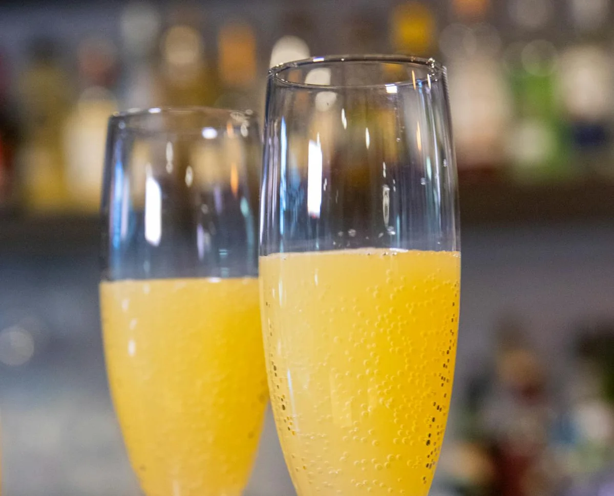Two champagne flutes filled with orange mimosa on a bar counter.