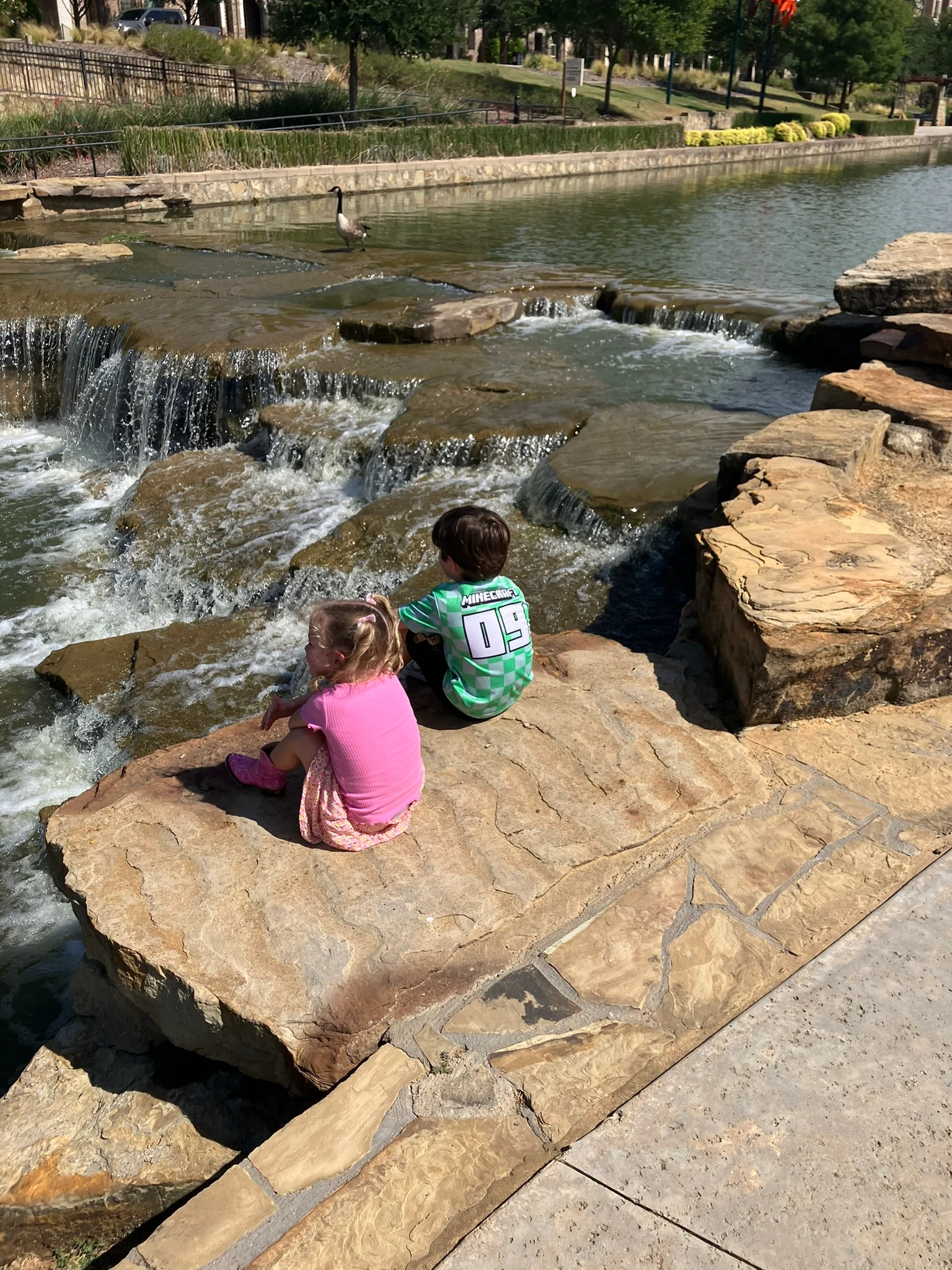 Children sitting by a serene waterfall in a park