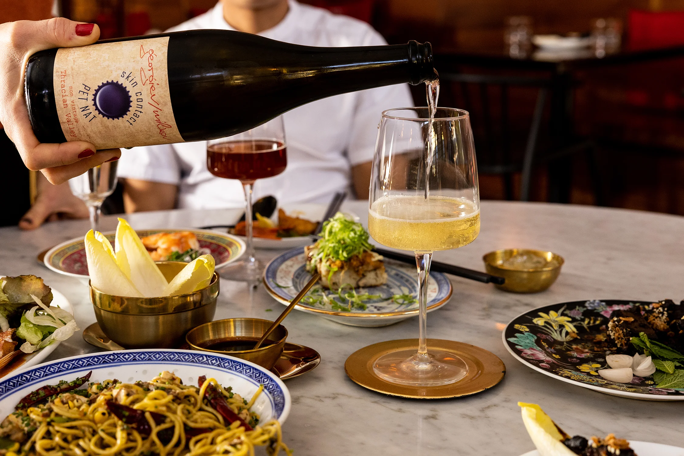 Pouring sparkling wine at a vibrant dining table with Asian-inspired dishes
