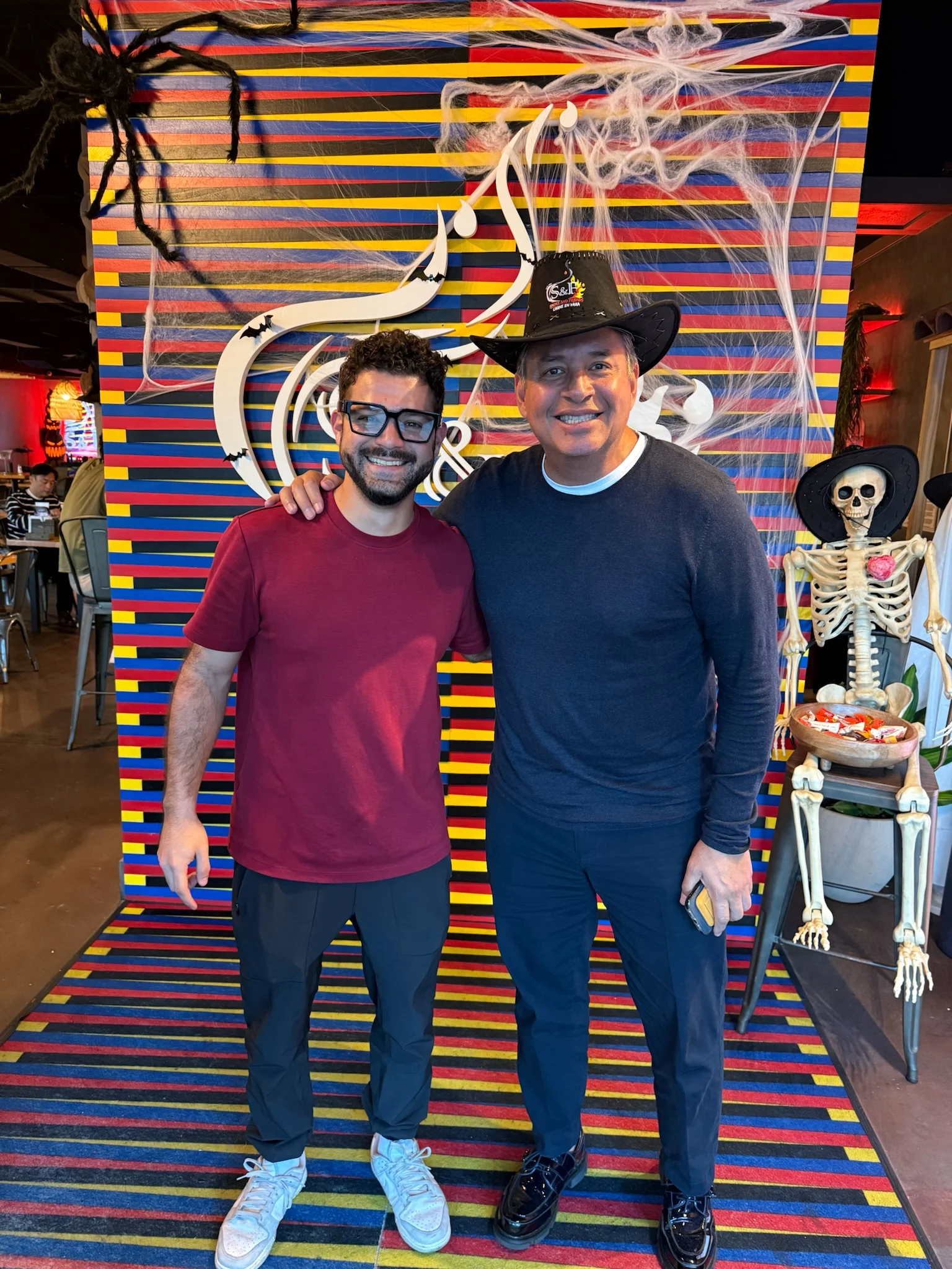 Two men posing in a vibrant restaurant with Halloween decor