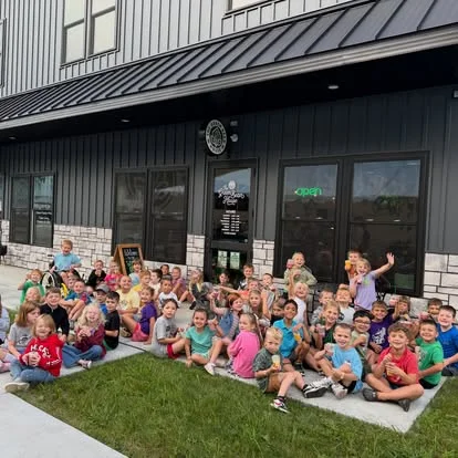 Group of children gathered outside a restaurant, smiling and waving
