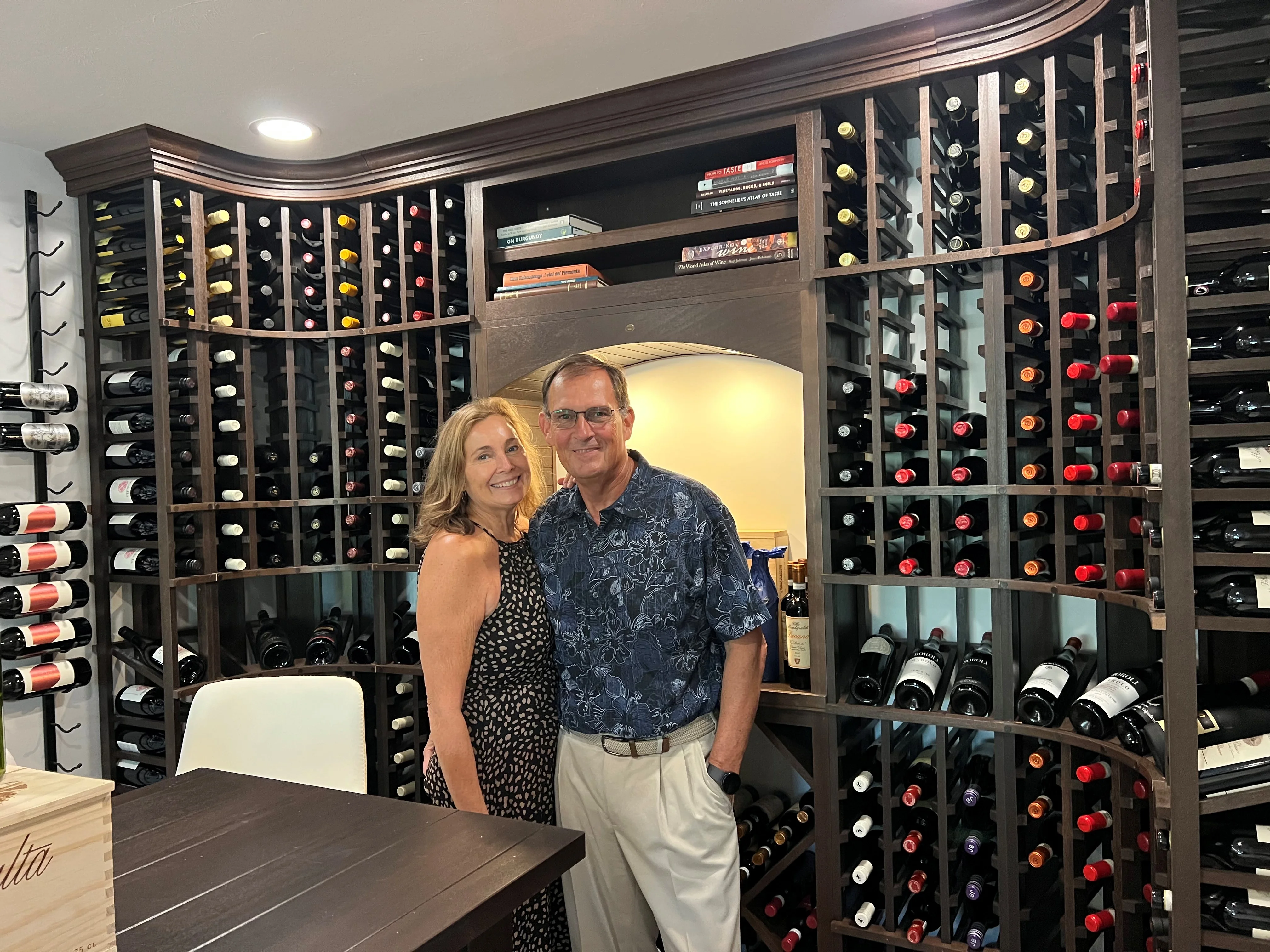 Couple smiling in a wine cellar with a collection of bottles.