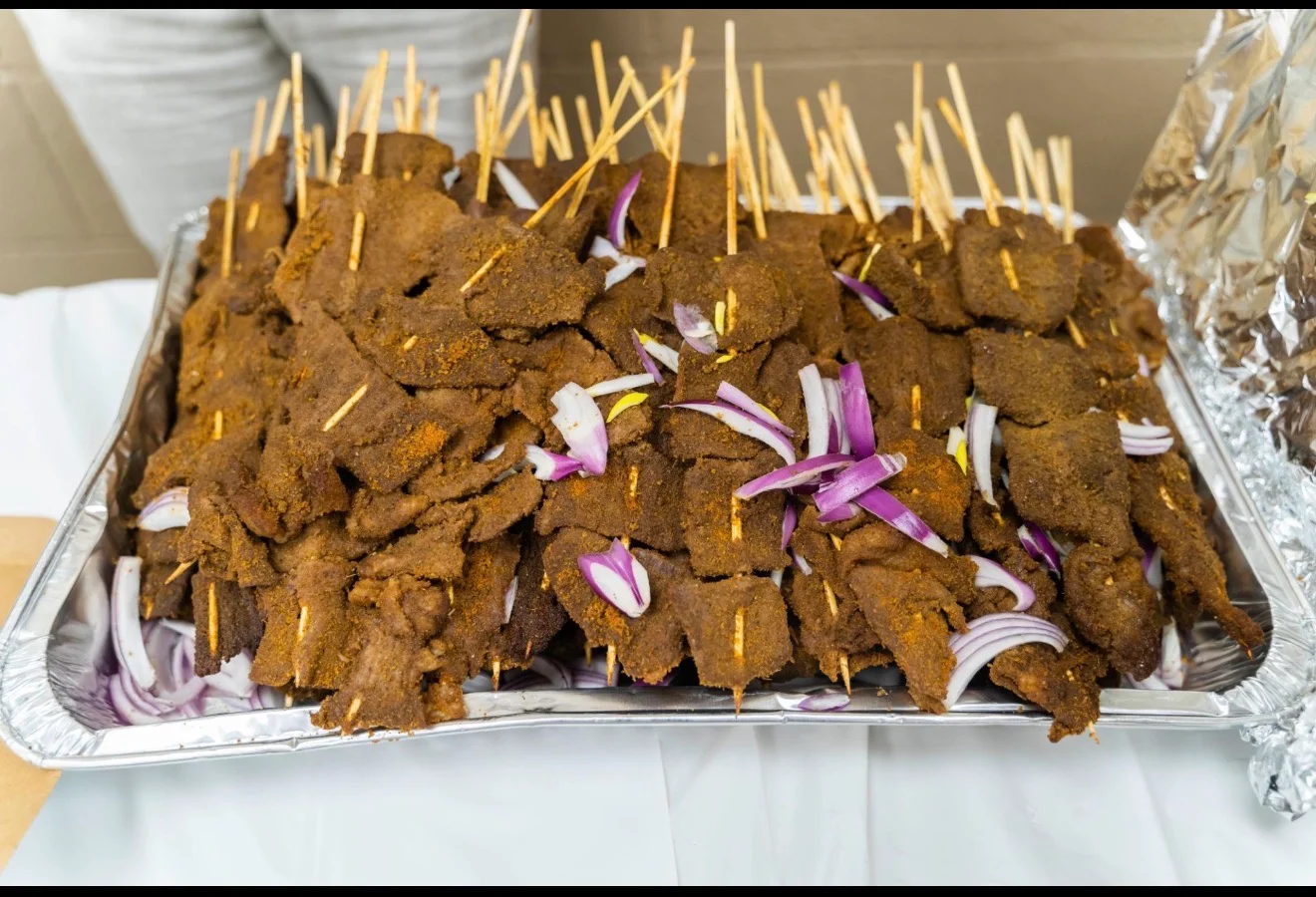 A large tray filled with grilled skewers of meat, seasoned and accompanied by slices of onion.