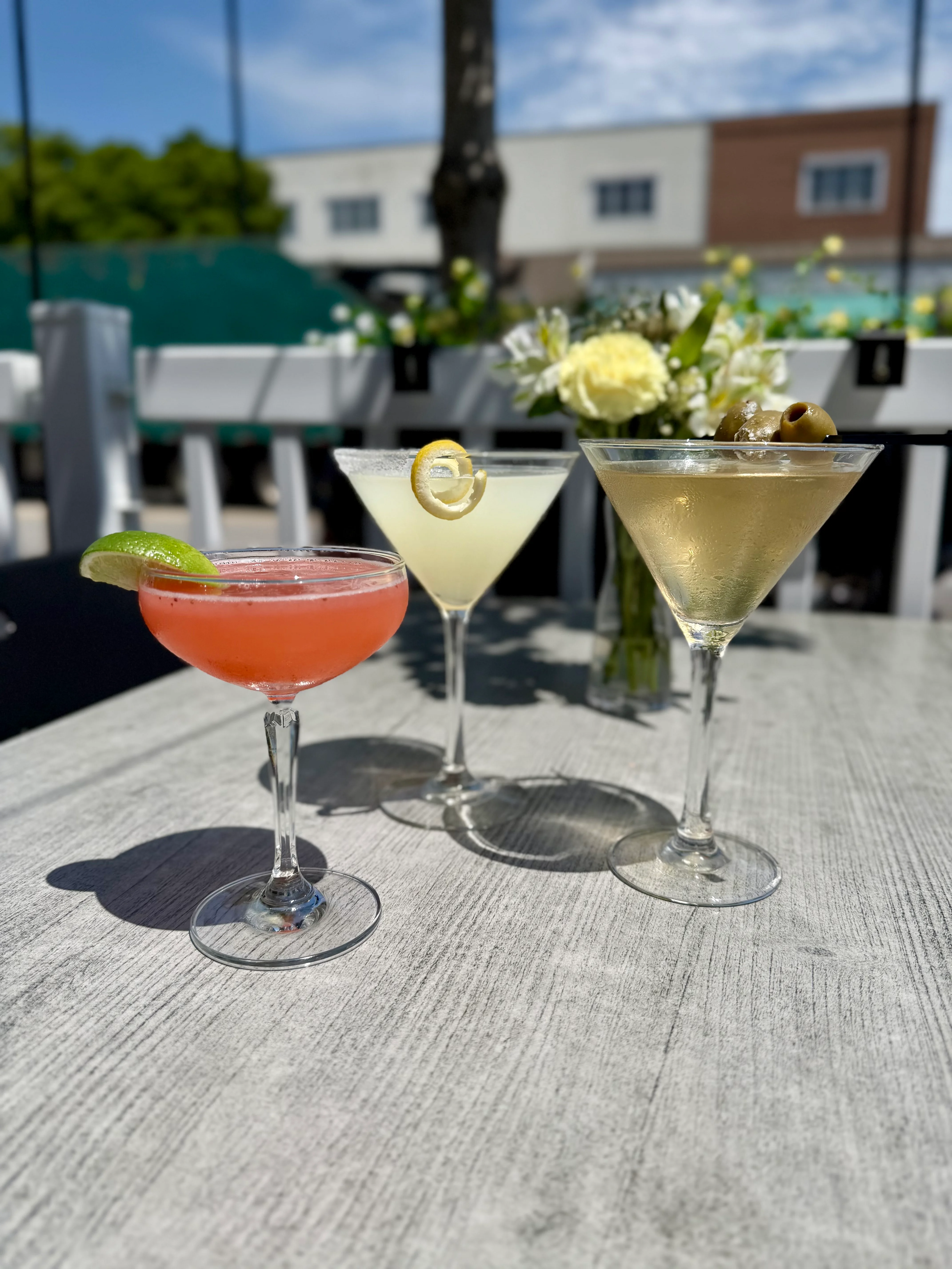 Three colorful cocktails on a sunny patio table