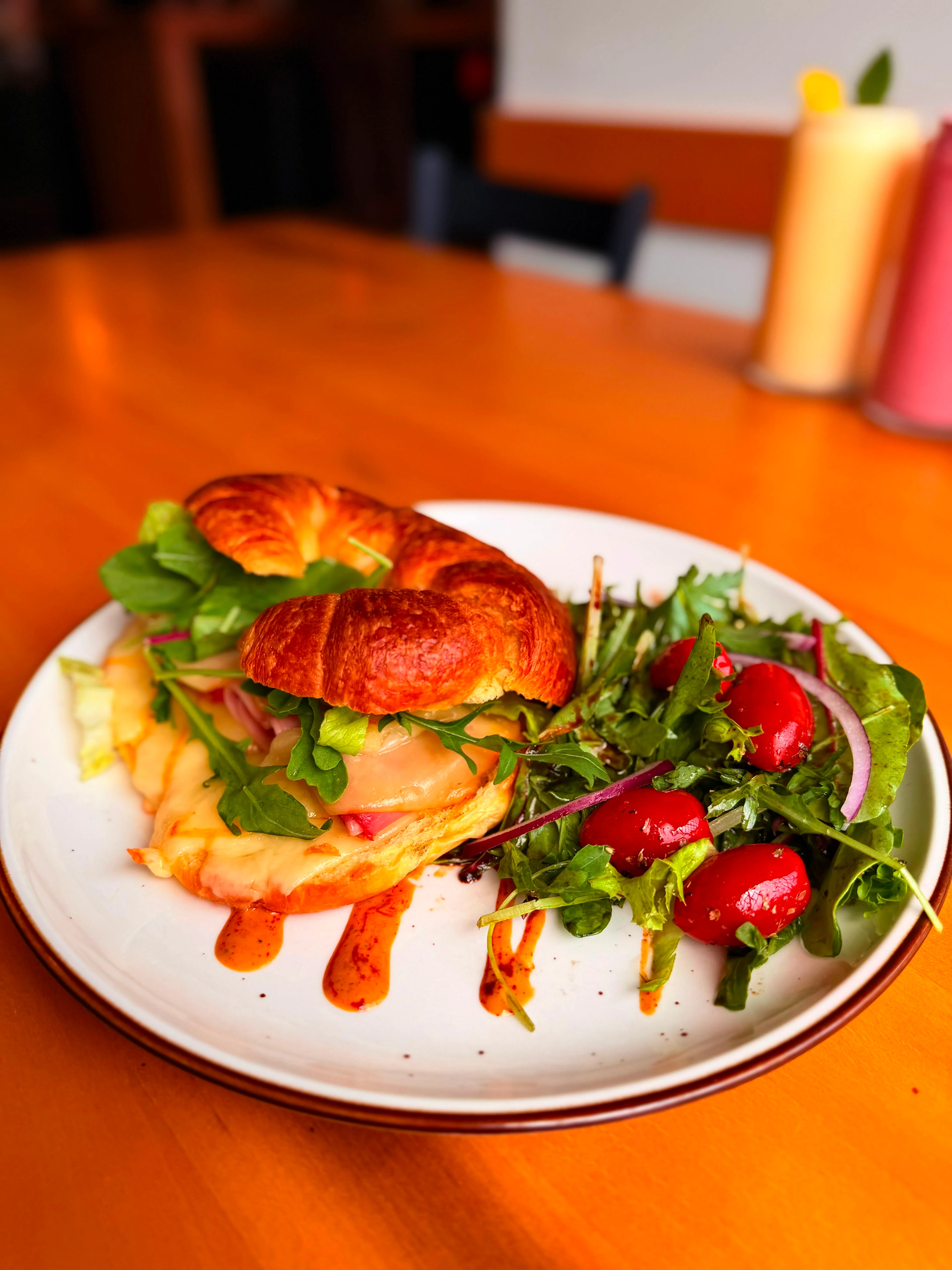 A croissant sandwich filled with cheese and ham, served alongside a fresh salad with cherry tomatoes on a white plate.