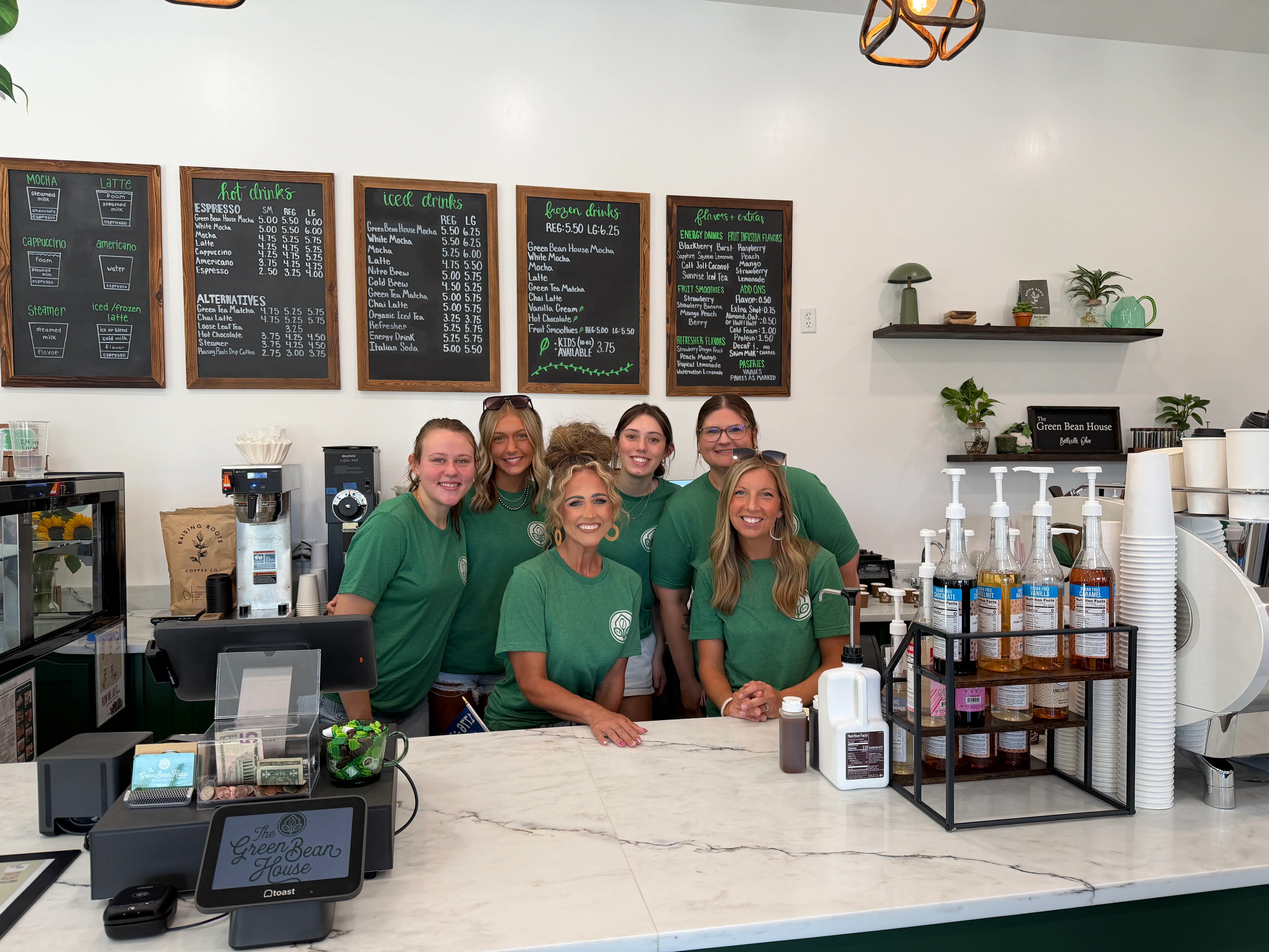 Friendly baristas at a coffee shop counter with menu boards in the background