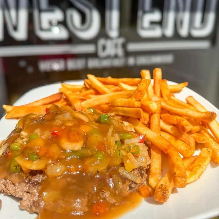 A plate featuring a savory beef dish topped with vegetables and gravy, accompanied by a side of golden French fries.