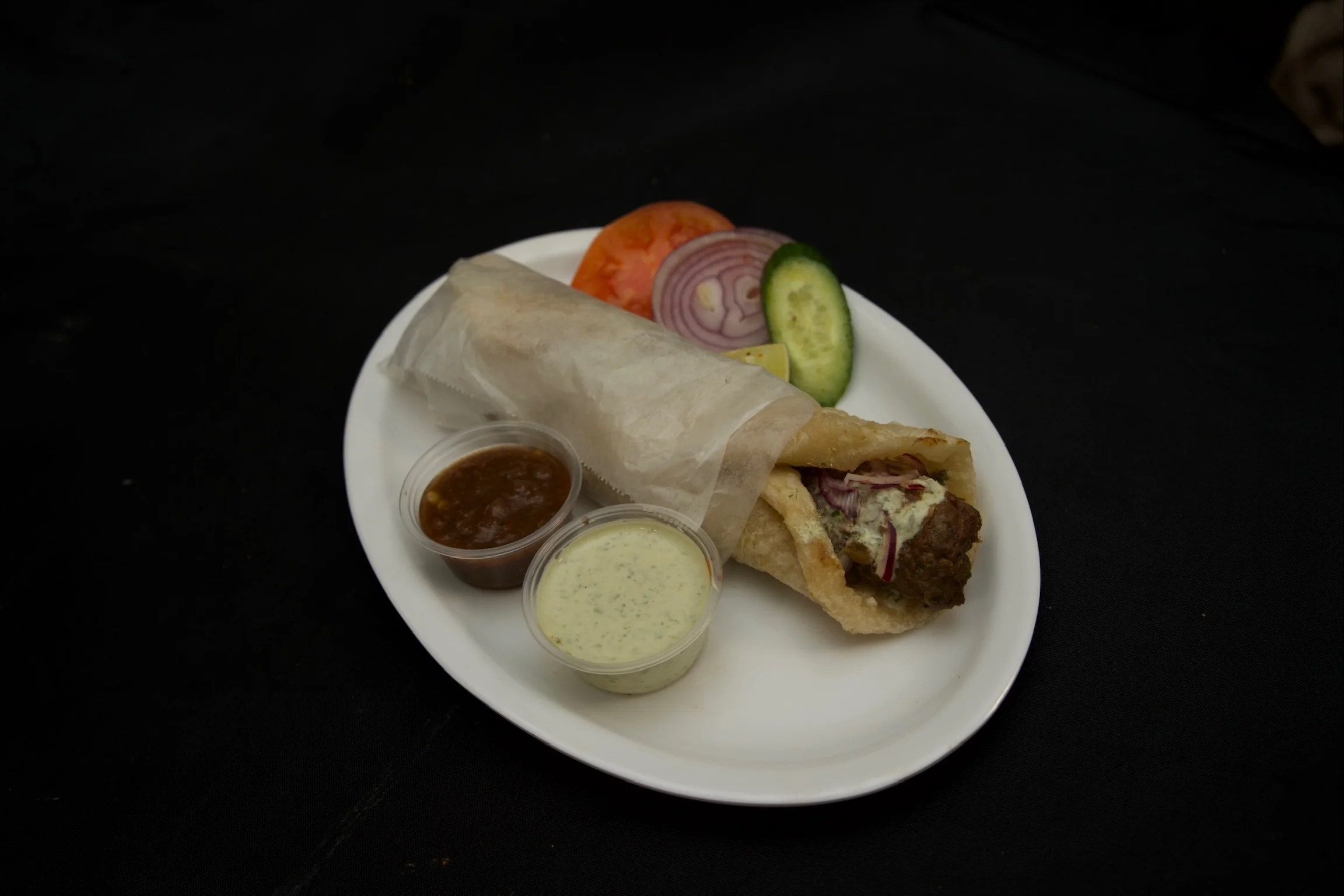 Beef seekh kabab paratha roll served with creamy garlic sauce, spicy chutney, and fresh salad at Karachi BBQ Tonight.