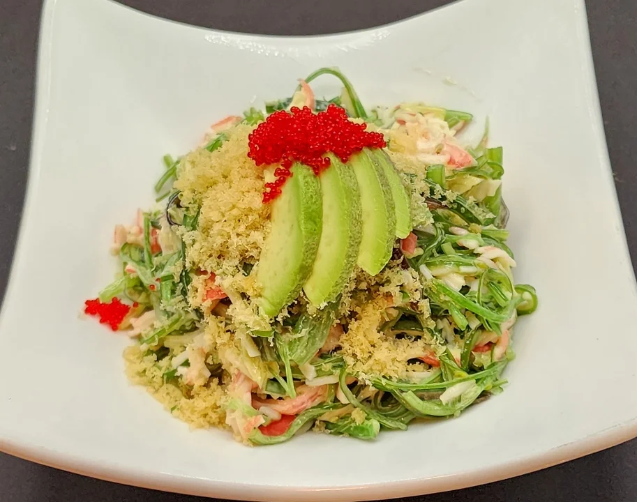 A vibrant salad featuring a mix of greens topped with slices of cucumber, fish roe, and shredded crab meat, garnished with crispy flakes.