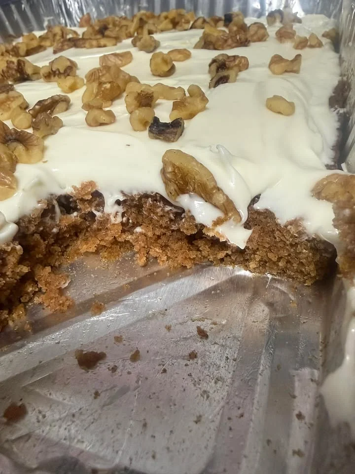 A slice of cake with cream frosting topped with walnuts, showcasing a rich brown interior.