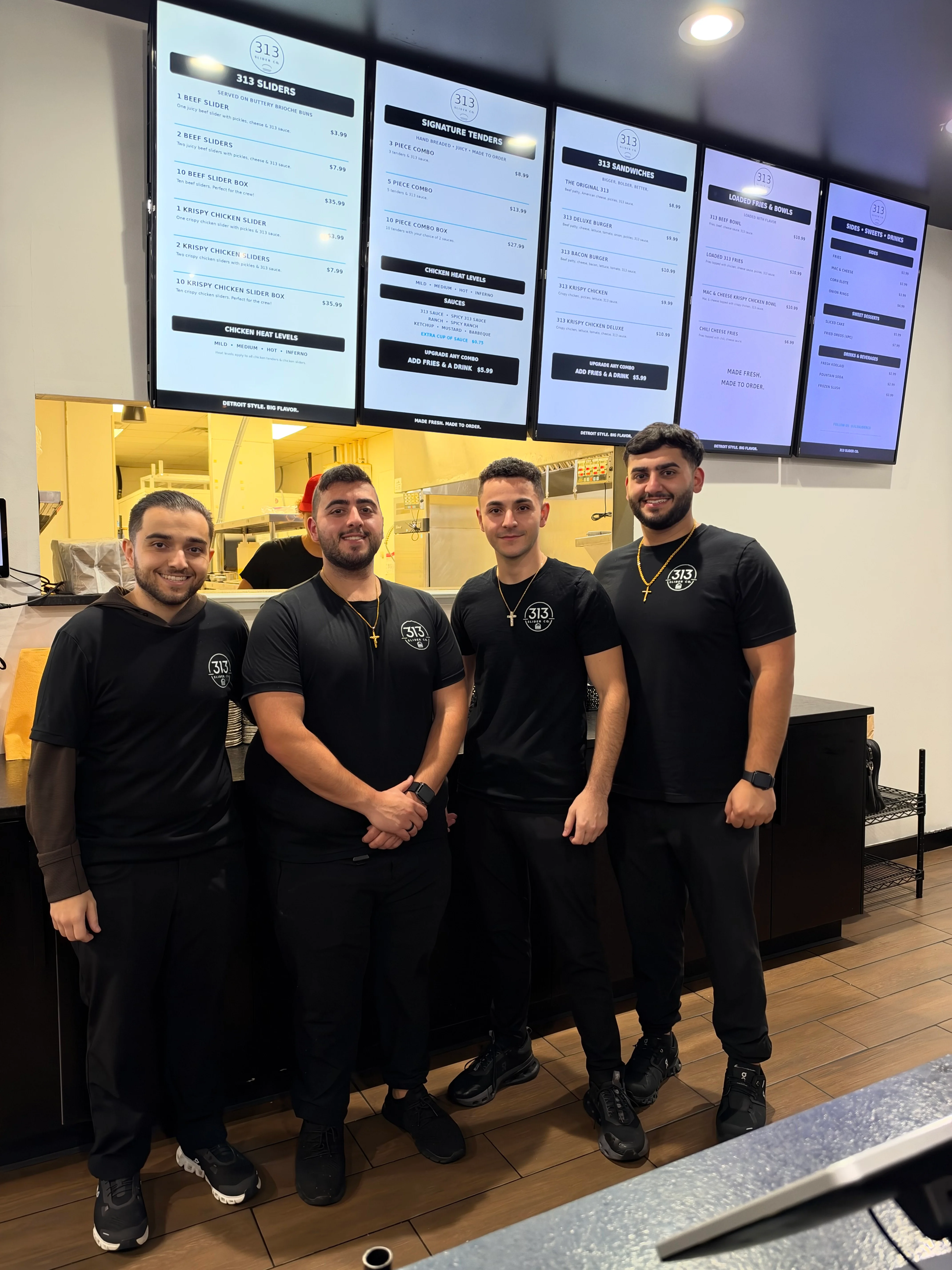 Restaurant staff posing beneath digital menu boards in a fast-casual dining room