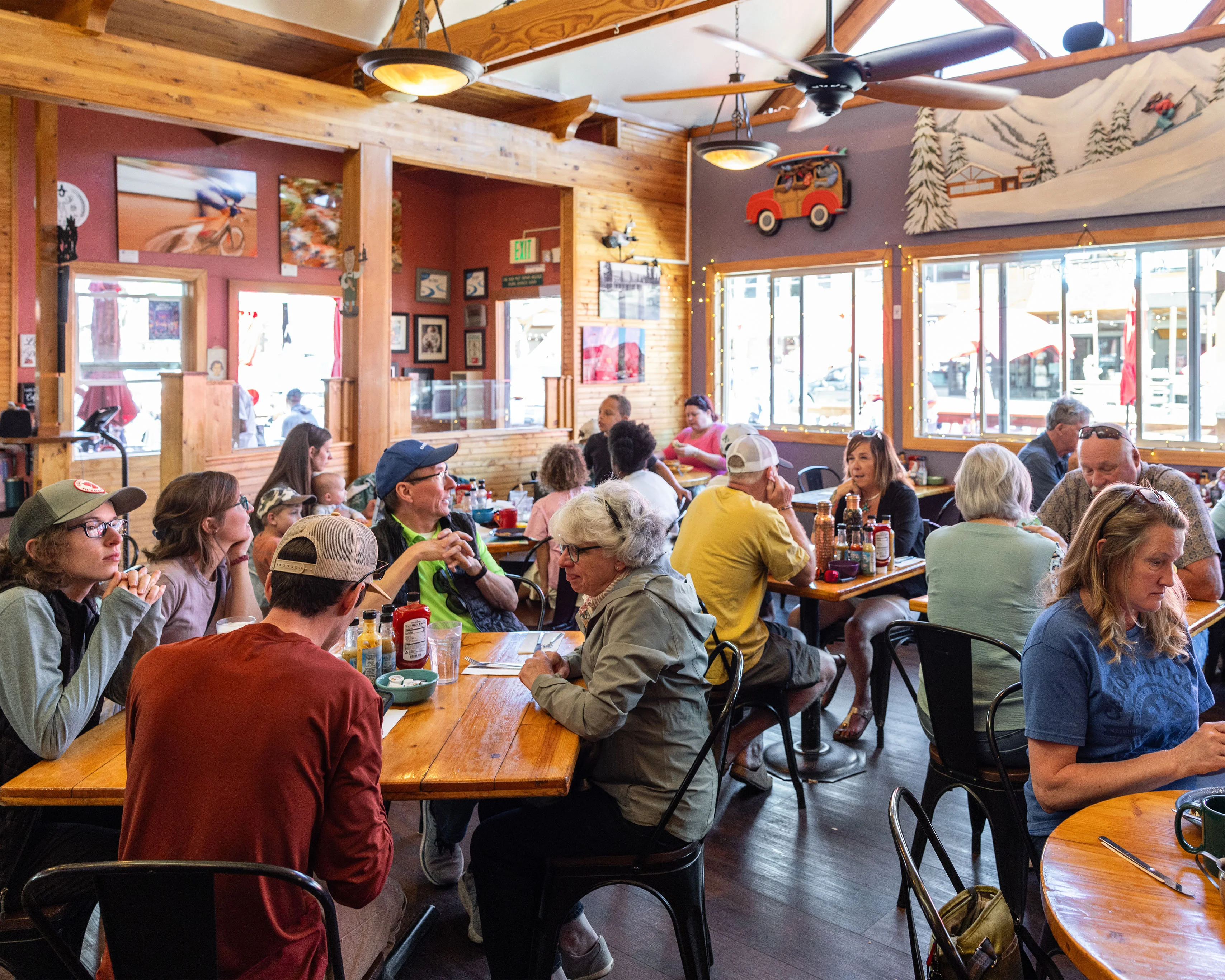 Busy rustic restaurant dining room with wood beams and mountain mural