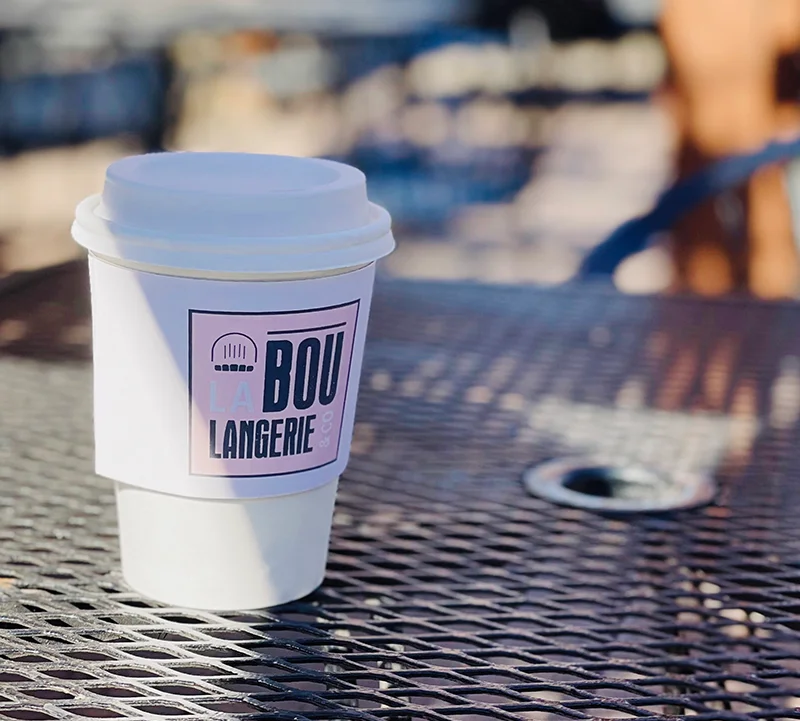 Coffee in custom La Boulangerie sleeve, symbolizing catering, markets, and French retail offerings.
