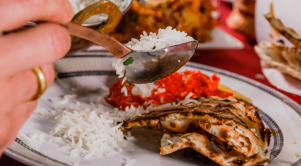 A close-up of a guest enjoying a meal at Mint Indian Restaurant in Denver, serving fluffy basmati rice onto a plate with fresh naan bread.