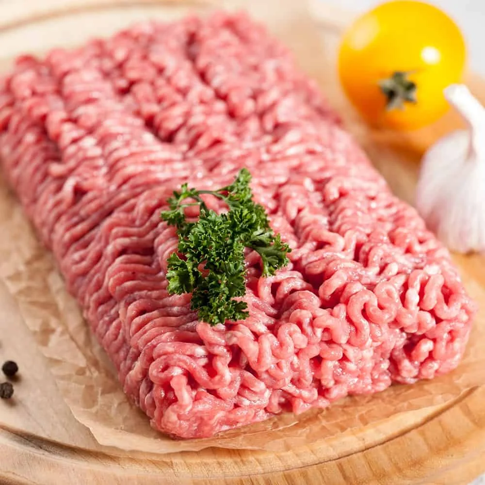 Plate of ground pork ready for cooking, garnished with herbs.