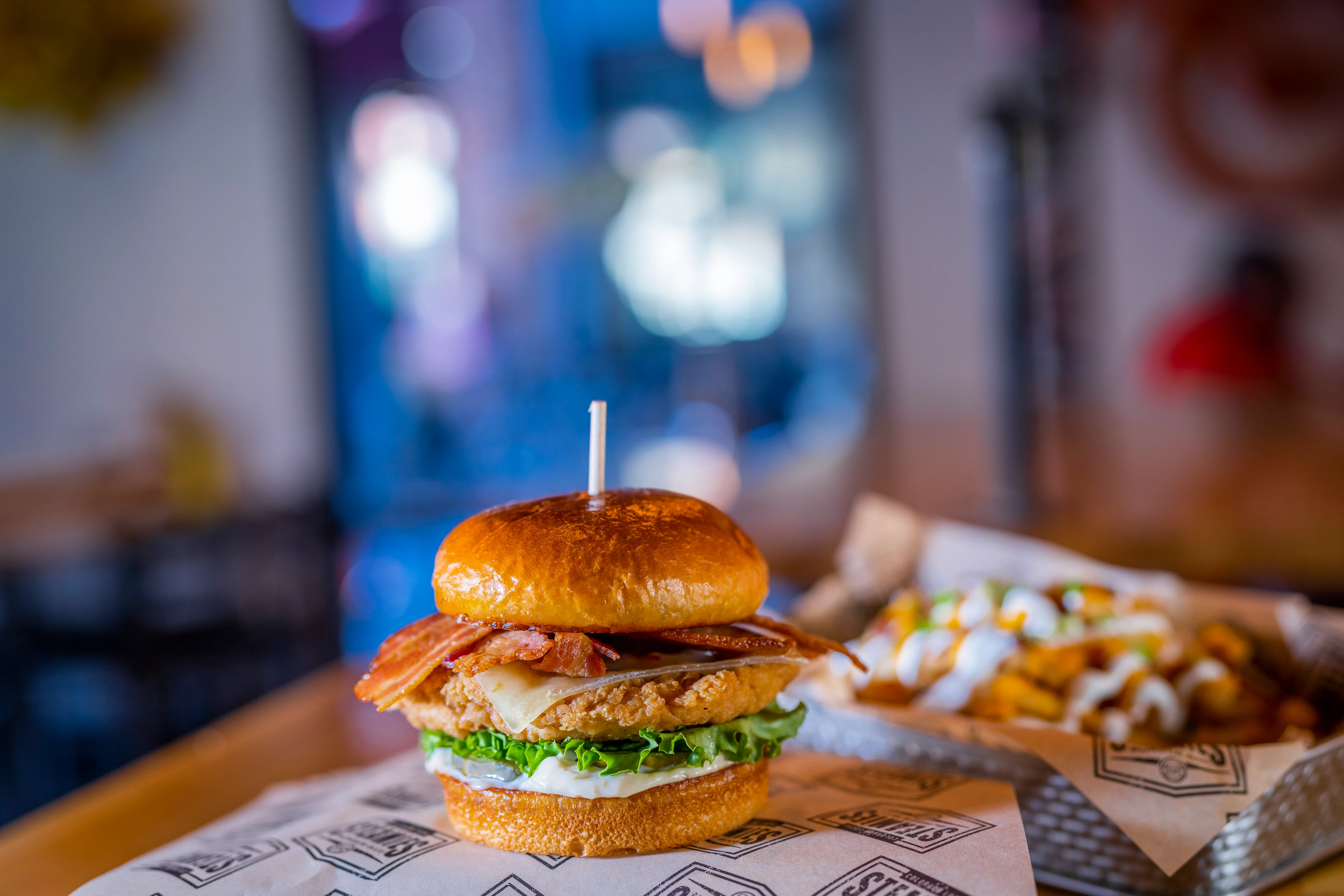 A delicious chicken sandwich topped with crispy bacon and fresh lettuce, served on a golden bun with a side of fries.