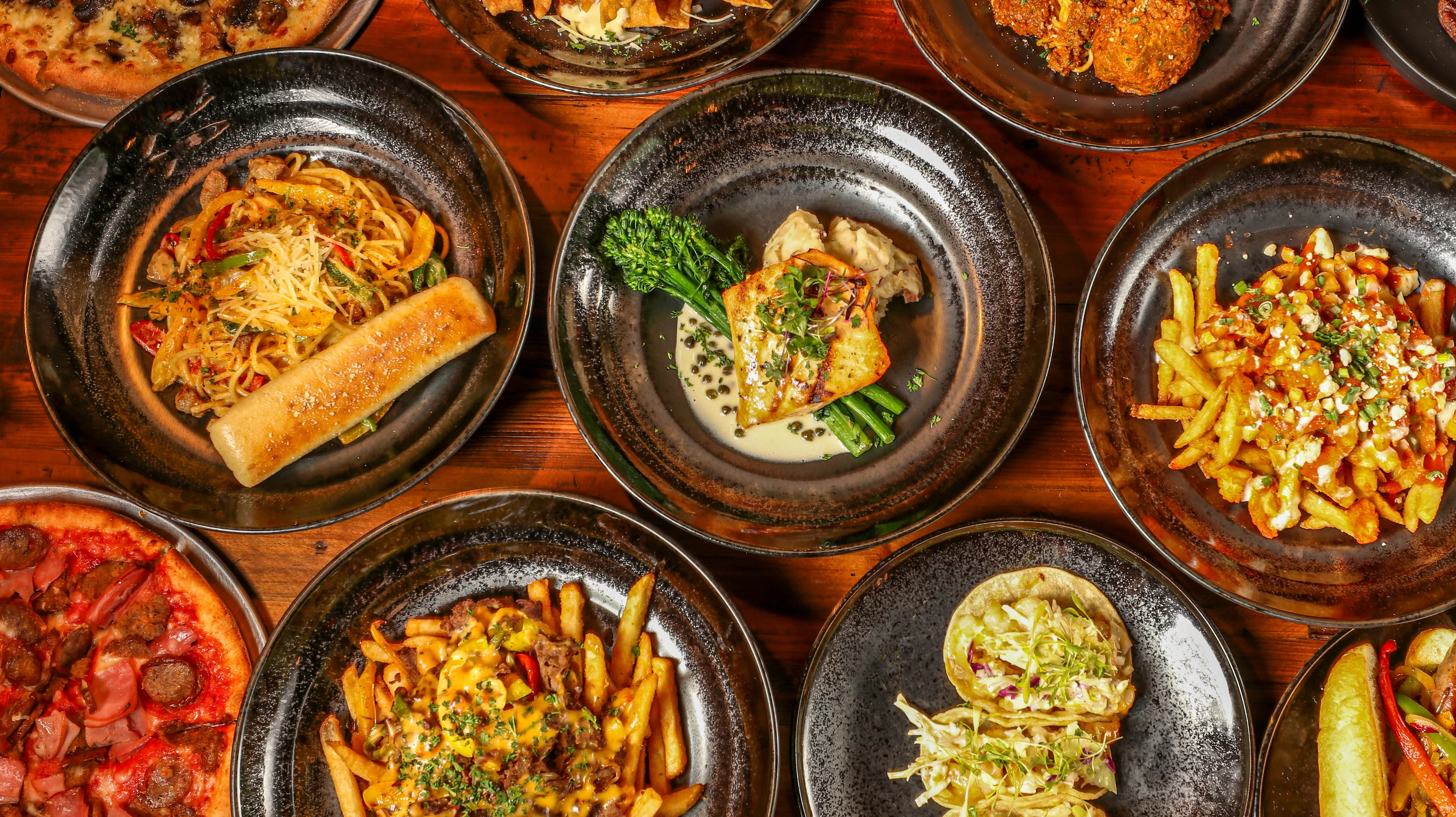 Variety of global dishes including pasta, pizza, and tacos on rustic wooden table