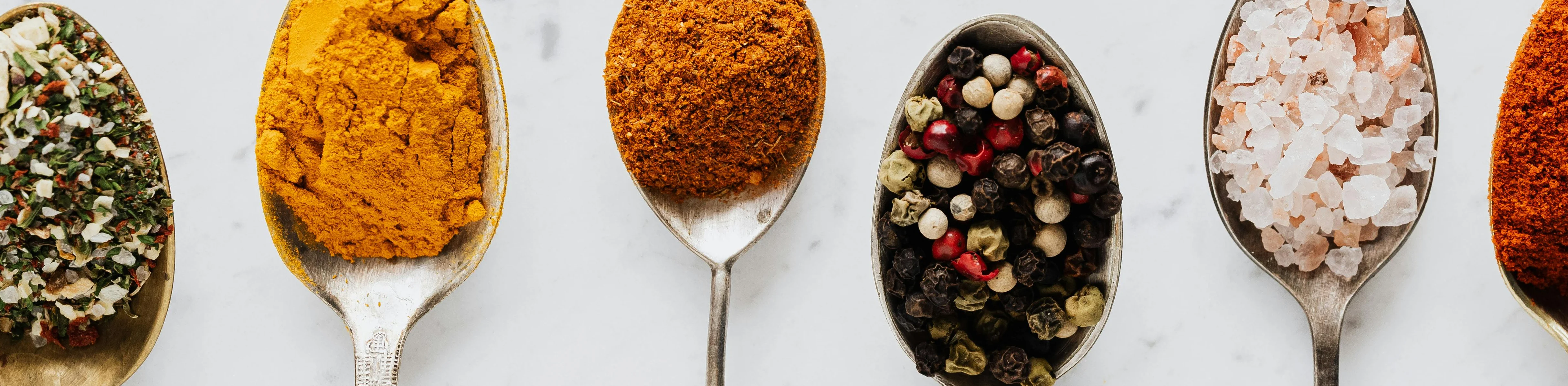 Variety of spices in vintage spoons on marble surface