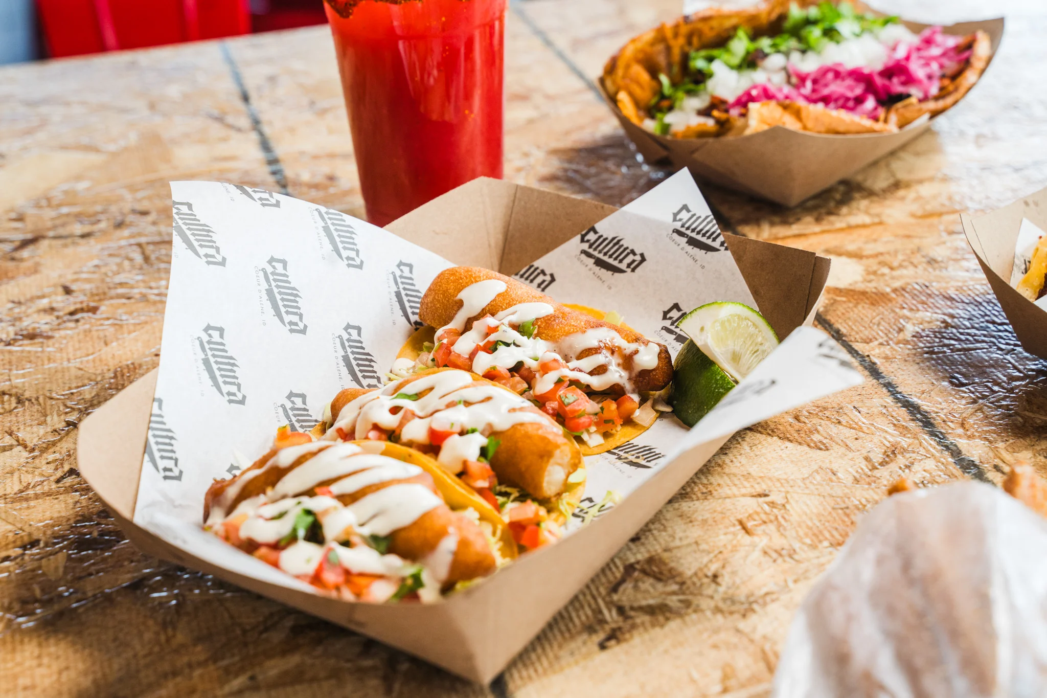Three tacos with toppings and a lime wedge on a wooden table.