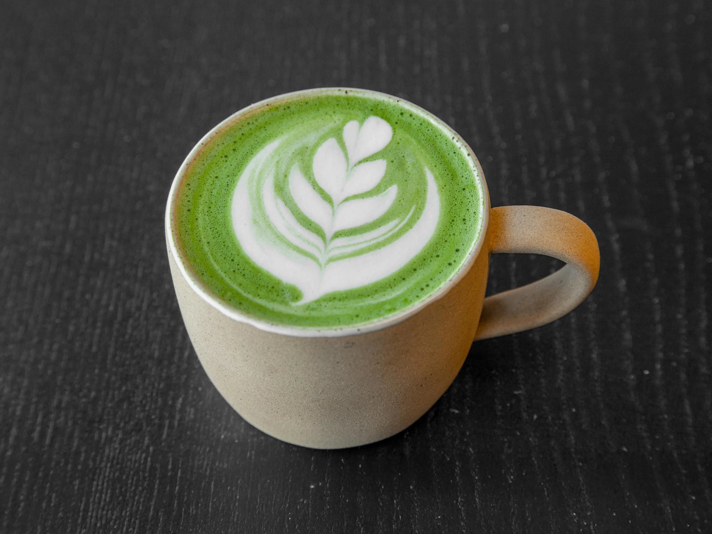 A matcha latte in a ceramic cup, beautifully topped with latte art in the shape of a leaf.