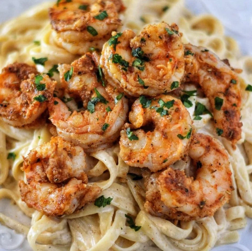 A plate of fettuccine pasta garnished with seasoned shrimp and fresh parsley.