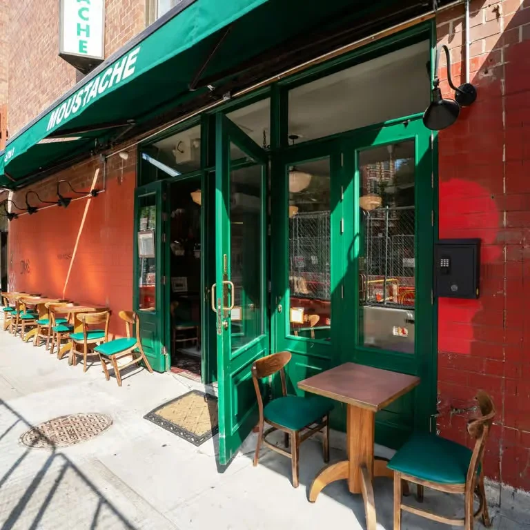 Exterior view of Moustache restaurant with green doors and outdoor seating.