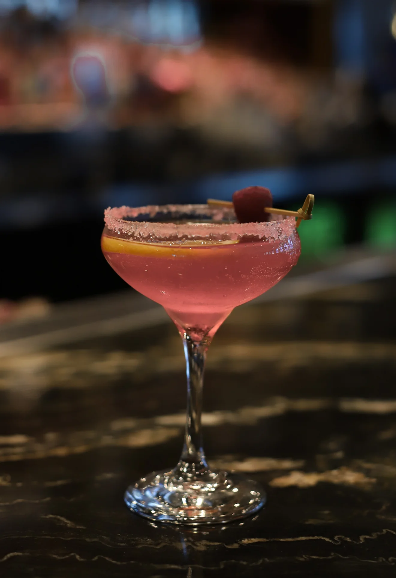 Vibrant pink cocktail with a sugared rim and garnish