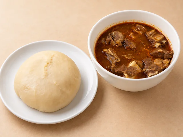 A serving of a traditional dish featuring a round, soft dough ball next to a bowl of rich meat stew with large chunks of meat.