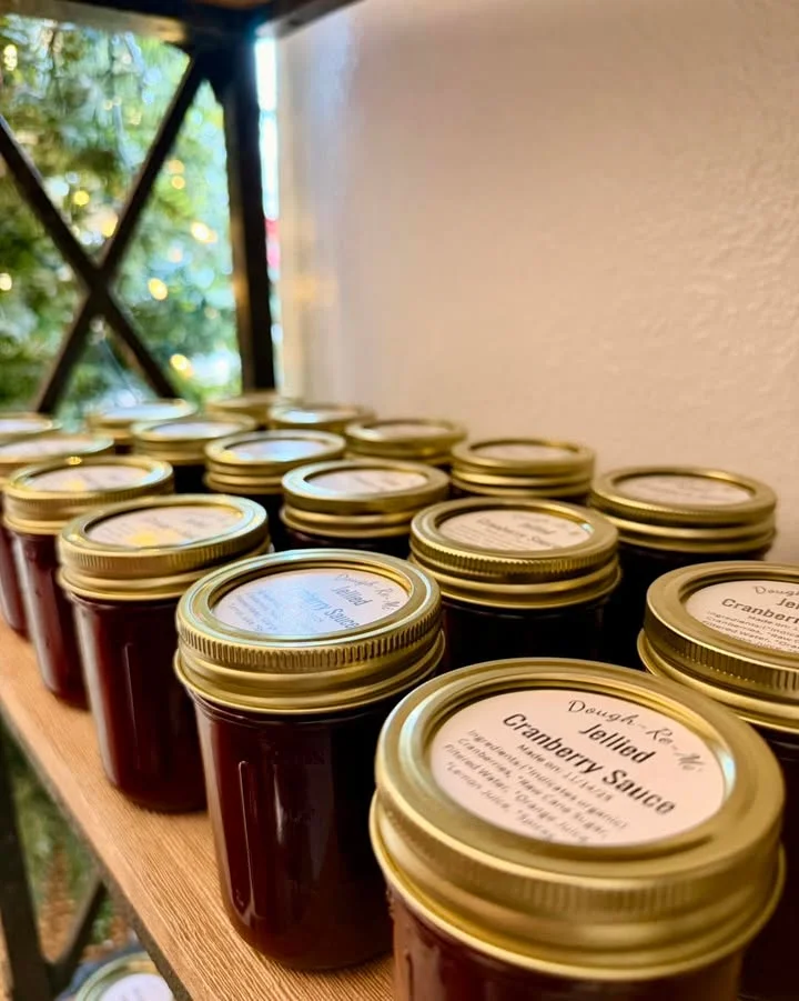 A collection of jars filled with cranberry sauce lined up on a shelf, each with a labeled lid.