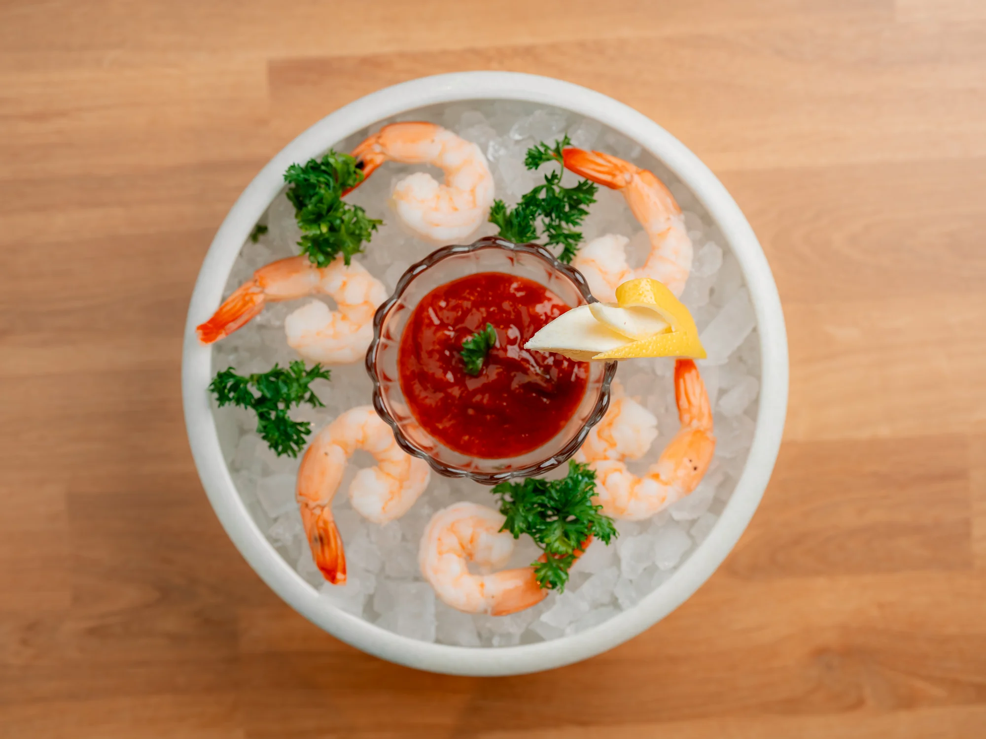 A chilled bowl of shrimp arranged around a cocktail sauce. The shrimp are garnished with parsley and served over ice.