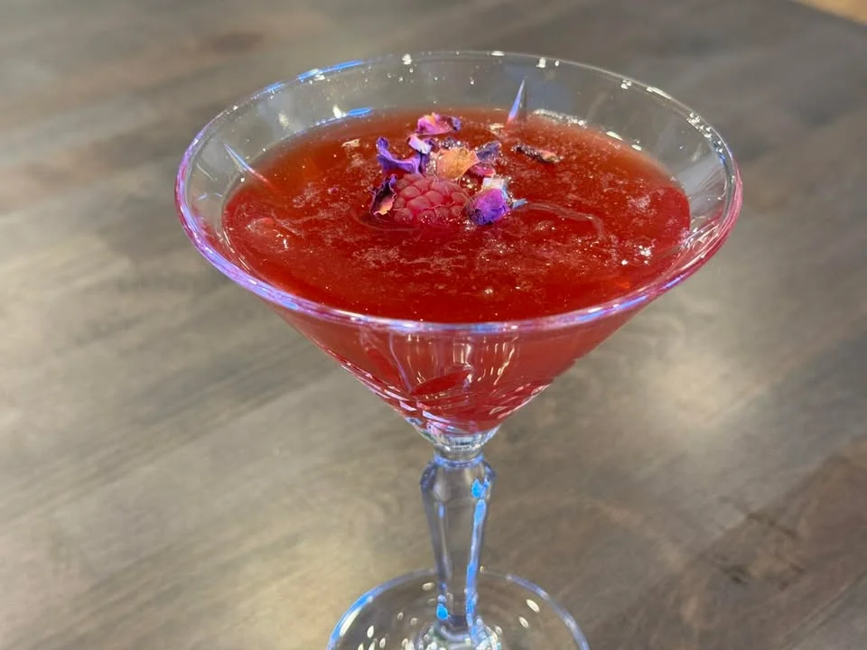 Elegant cocktail garnished with flowers and raspberries