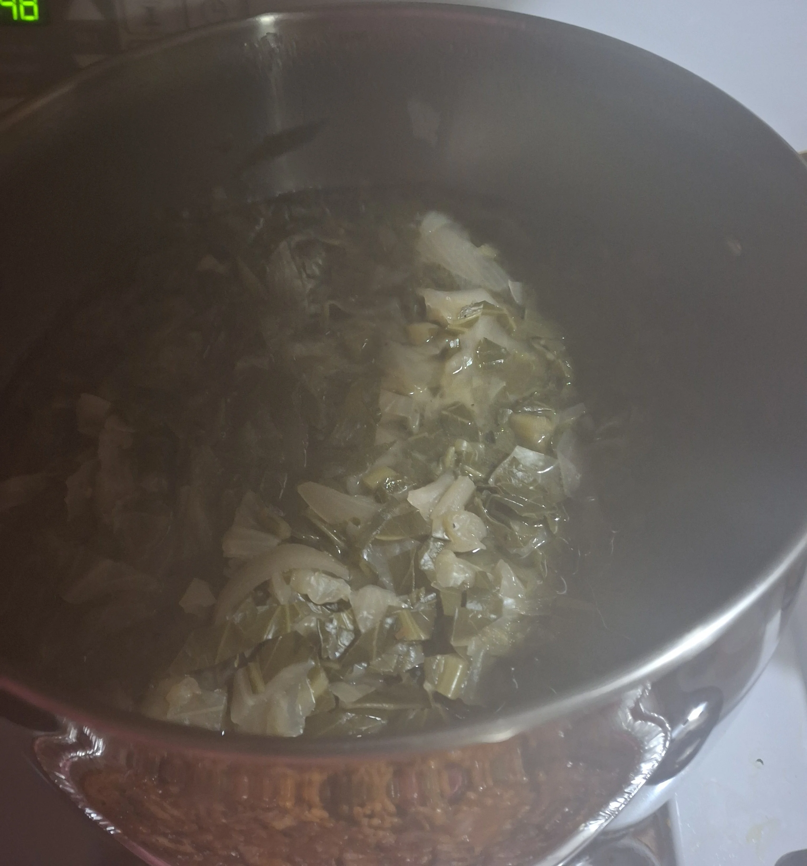 A pot of leafy greens boiling in water, creating steam above the surface.