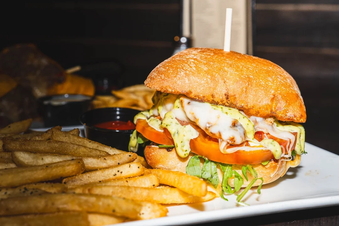 A fresh sandwich with layers of lettuce, tomato, and cheese on toasted bread, accompanied by a side of fries and dipping sauce.