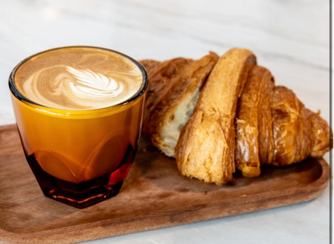Café au lait with a buttery croissant on a wooden tray