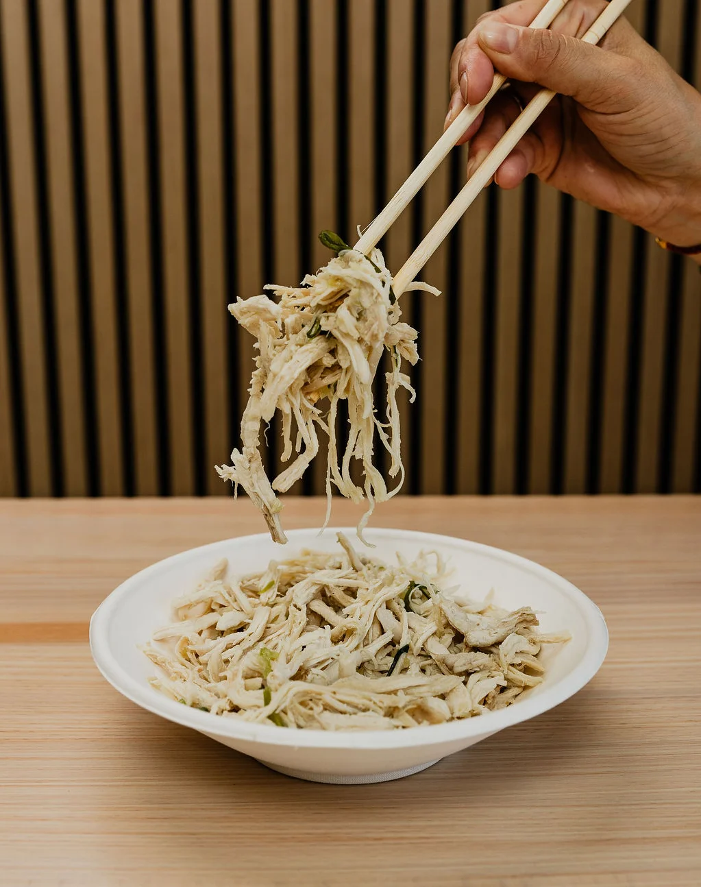a hand holding up a portion of juicy hand pulled ginger scallion chicken with chopsticks