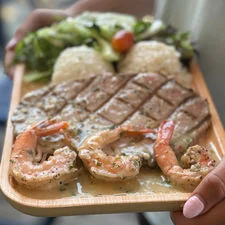 Grilled steak and shrimp served with rice and salad on a wooden platter.