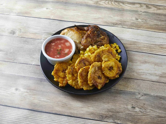 Plate of roasted chicken, fried plantains, corn, and tomato sauce.