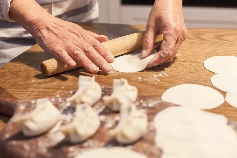 Homemade Chinese dumplings being rolled out on a wooden surface