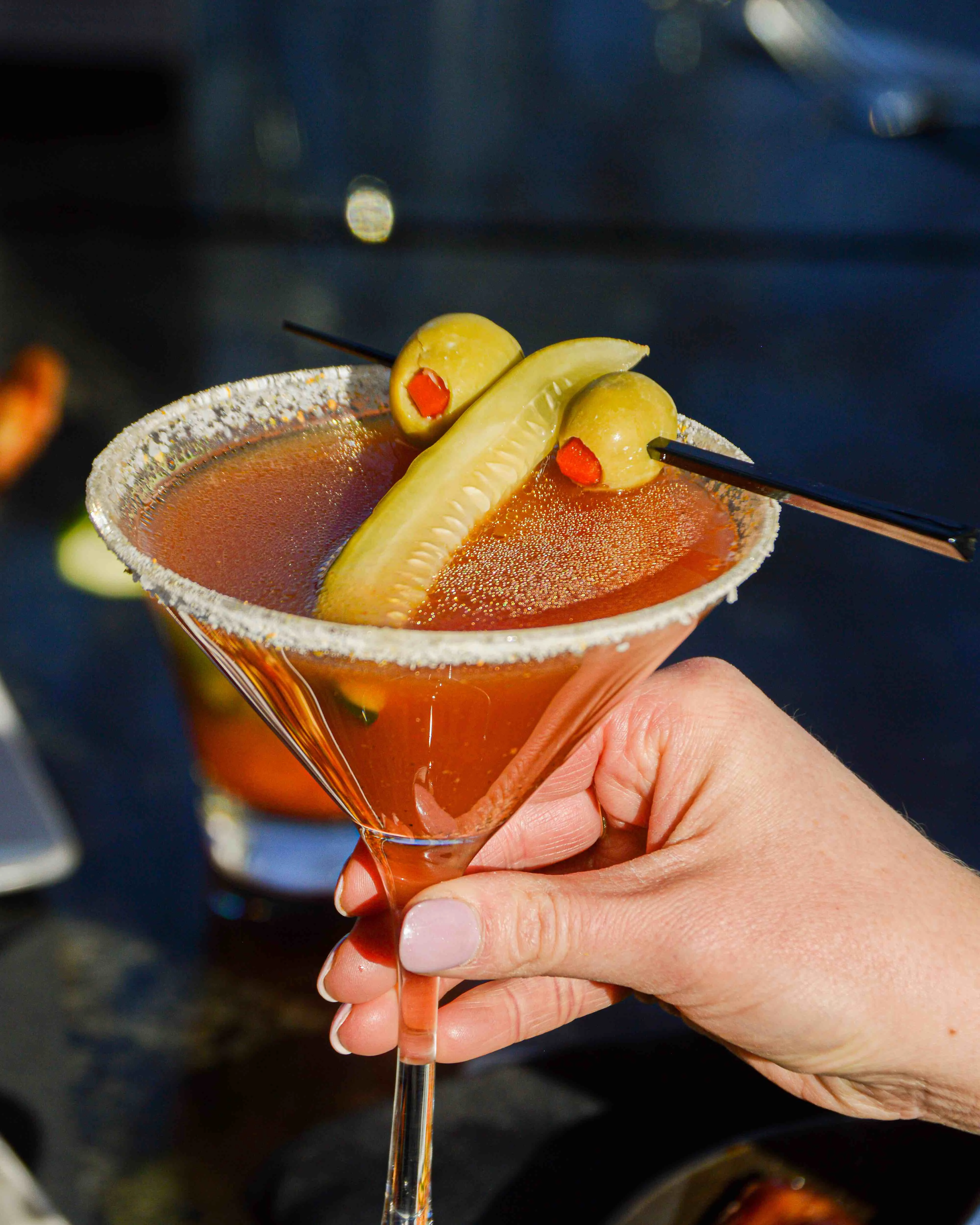Naughty Pickle Martini being held in front of some bright lights 
